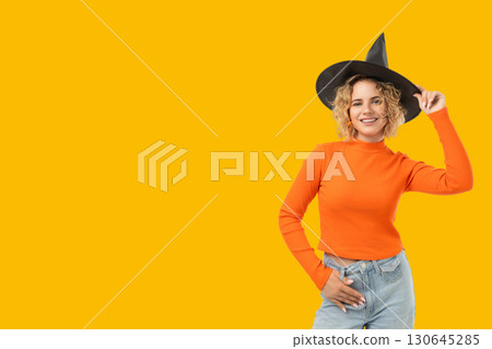 Cheerful woman in orange sweater and witch hat enjoying Halloween 130645285