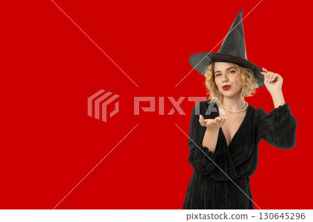 Woman in black dress and witch hat blows celebratory kiss 130645296