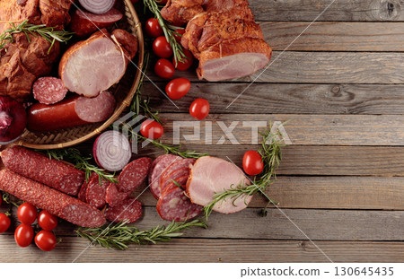 Food tray with delicious salami, ham, fresh sausages, tomato, and rosemary. 130645435