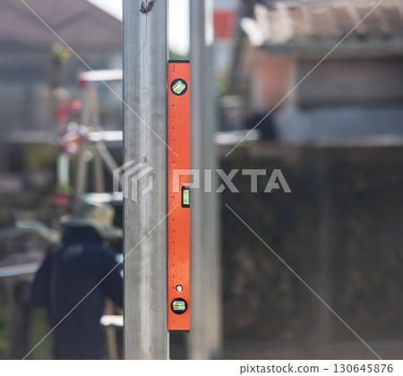 Construction worker use spirit level and measures the vertical of the iron pole in site. 130645876