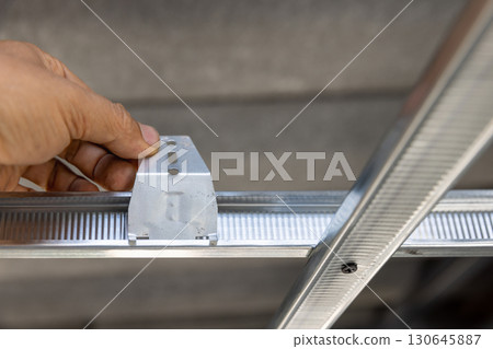 Worker is using  locking keys to lock top cross rails to furring channels in concealed ceiling 130645887