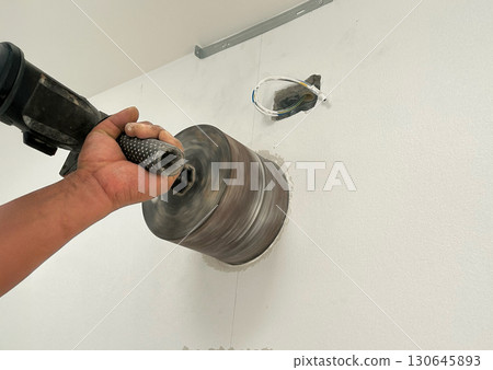 Worker Drilling kitchen wall to mounted hood air duct. 130645893