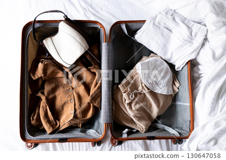 Open suitcase with casual clothing and accessories for travel on white bed Open suitcase with casual clothing and accessories for travel on white bed 130647058