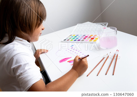 Young caucasian child painting with watercolors at a white table Young caucasian child painting with watercolors at a white table 130647060