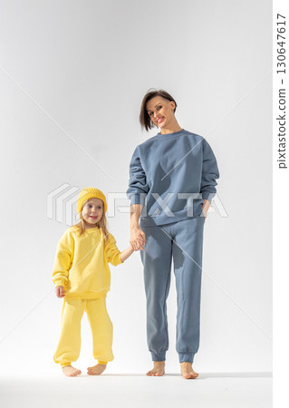 Young mother and little daughter walking holding hands. Dressed in yellow and ment color suits on white background, studio. Concept of Mother's Day love family, parenthood childhood. 130647617