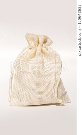 Beige burlap gift bag with drawstring tied on neutral background 130648682