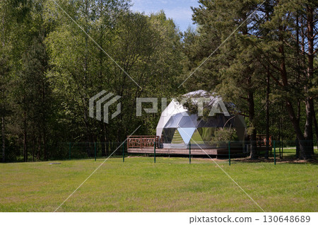 Geodesic dome in verdant forest clearing with lush greenery and sky view 130648689