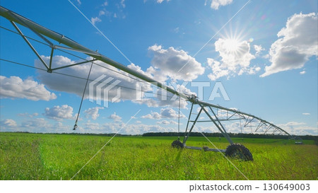 The irrigation system is operating in a lush green field that is situated beneath a bright sky The irrigation system is operating in a lush green field that is situated beneath a bright sky 130649003
