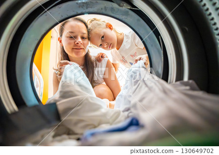 Mother and daughter doing laundry together in a self-service public laundromat, sharing household chores, building responsibility and cooperation in everyday family routine Mother and daughter doing laundry together in a self-service public laundromat, sharing household chores, building responsibility and cooperation in everyday family routine 130649702