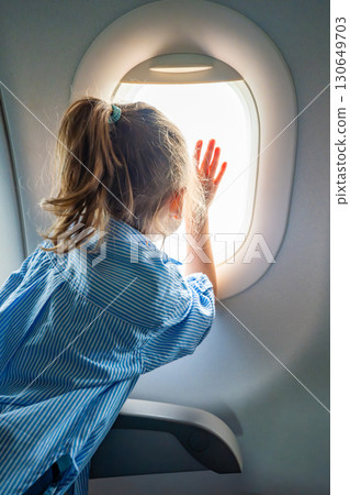 Little girl looking out the airplane window during a flight. Wonder, travel experience, and childhood curiosity in the air. 130649703