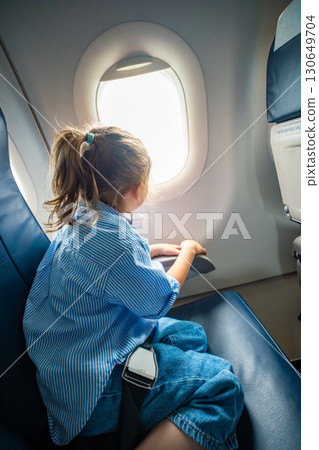 Little girl looking out the airplane window during a flight. Wonder, travel experience, and childhood curiosity in the air. Little girl looking out the airplane window during a flight. Wonder, travel experience, and childhood curiosity in the air. 130649704