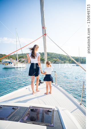 Mother and daughter spending time together on the bow of a sailing yacht. Family bonding, sea adventure, and peaceful travel lifestyle 130649715