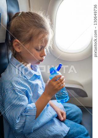 Little girl drinking water from a plastic bottle during a flight. In-flight hydration, travel routine, and caring for body needs while flying 130649736