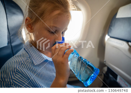 Little girl drinking water from a plastic bottle during a flight. In-flight hydration, travel routine, and caring for body needs while flying Little girl drinking water from a plastic bottle during a flight. In-flight hydration, travel routine, and caring for body needs while flying 130649748