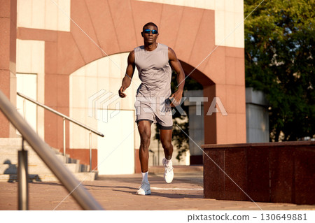Man running outdoors in athletic gear with urban architecture background Man running outdoors in athletic gear with urban architecture background 130649881