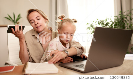 Mother multitasking with child while working remotely from home office Mother multitasking with child while working remotely from home office 130649885