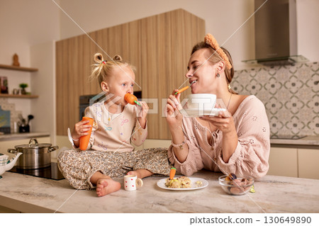 Mother and daughter enjoying a cheerful moment while eating together in a kitchen 130649890