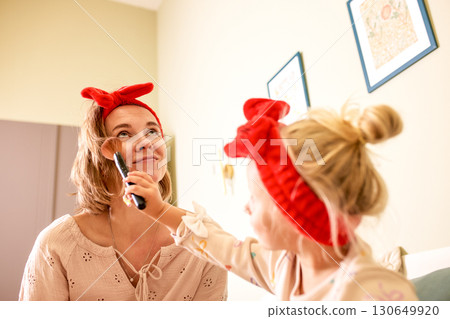 Mother and daughter enjoying a playful makeup session in a home setting 130649920
