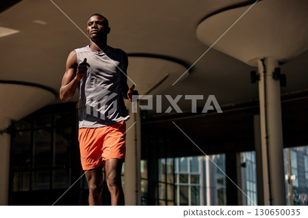 Athletic man jogging outdoors under modern urban architecture and daylight 130650035