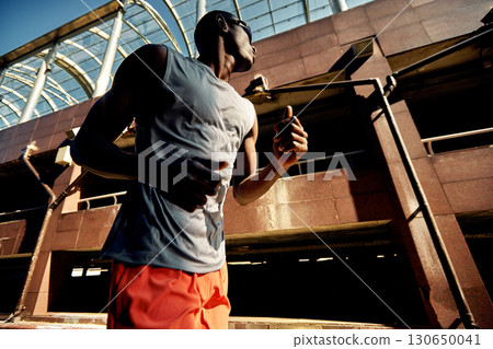 Man running outdoors under modern urban architecture during sunny day 130650041