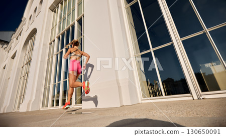 Woman jogging by a modern building with glass windows under the sun 130650091