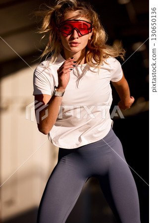 Athletic woman running outdoors in the sunlight wearing red sport sunglasses Athletic woman running outdoors in the sunlight wearing red sport sunglasses 130650136