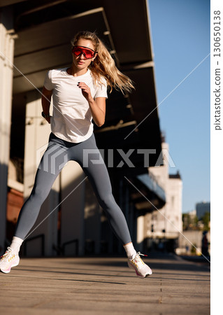 Athletic woman exercising outdoors under bright sunlight wearing sportswear and sunglasses Athletic woman exercising outdoors under bright sunlight wearing sportswear and sunglasses 130650138
