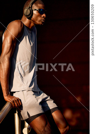 Athletic man resting in sunlight, wearing headphones in casual workout attire 130650209
