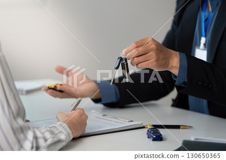 Key Handover. Professional presenting car keys to client during insurance consultation. 130650365