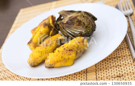 cooked fried chicken wings and halves artichokes on white plate 130650935