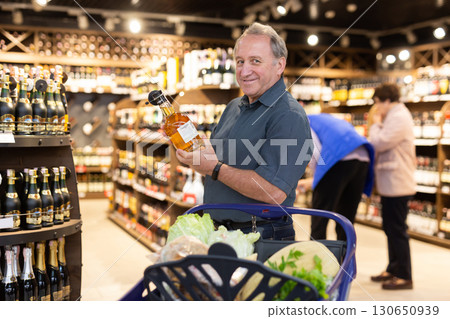 Elderly man choose bottle of alcohol 130650939