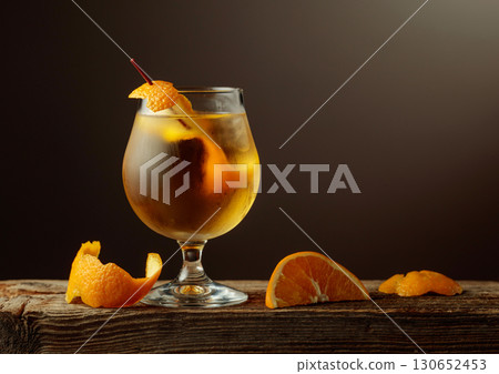 Old Fashioned cocktail with a ice, garnished with an orange peel on a old wooden board. Old Fashioned cocktail with a ice, garnished with an orange peel on a old wooden board. 130652453