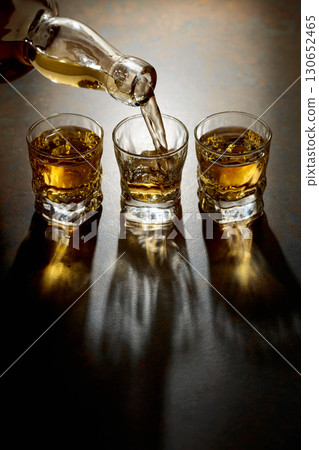 Whiskey pour from a bottle into a small glasses. 130652465