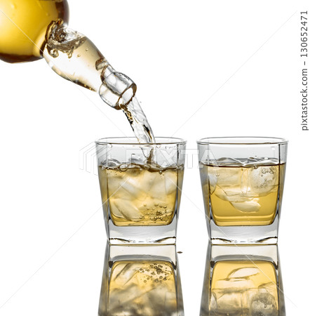 Pouring Whiskey from a bottle into a glass with ice on a white background. 130652471