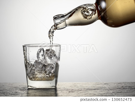 Whiskey is poured from a bottle into a glass with ice. Whiskey is poured from a bottle into a glass with ice. 130652473