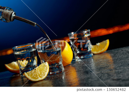 Vodka and lemon slices on a dark blue background. 130652482