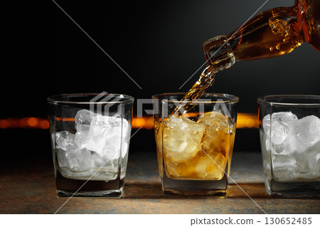 Whiskey is poured into a glass with ice. Whiskey is poured into a glass with ice. 130652485