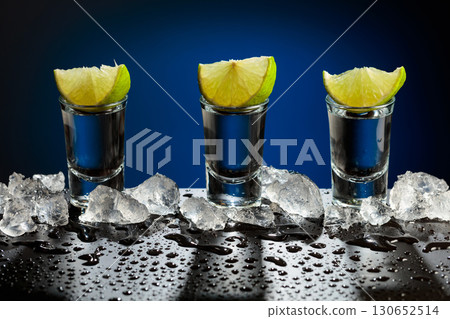 Tequila shots with lime slices on a wet black table. Tequila shots with lime slices on a wet black table. 130652514