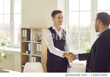 Two business men standing in office making deal shaking hands celebrating business achievement. Two business men standing in office making deal shaking hands celebrating business achievement. 130653026