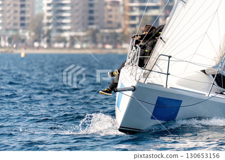 Sailors maneuvering a sailboat during a competitive regatta near the city coastline Sailors maneuvering a sailboat during a competitive regatta near the city coastline 130653156