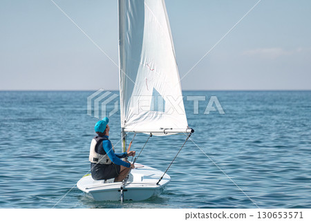 Sportsman steering dinghy sailing boat on calm sea Sportsman steering dinghy sailing boat on calm sea 130653571