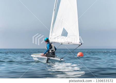 Sportsman steering dinghy sailing boat on calm sea 130653572