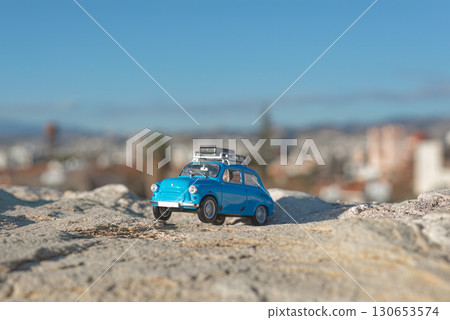 Blue toy car exploring a rocky hill overlooking a blurry city Blue toy car exploring a rocky hill overlooking a blurry city 130653574