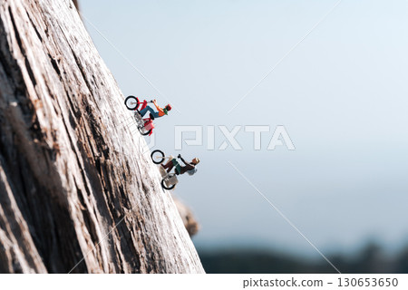 Miniature people riding motorcycles up a steep cliff face with copy space 130653650