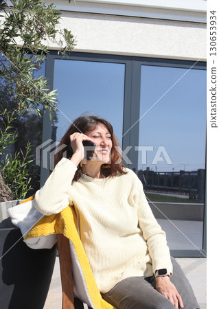 an adult woman on terrace making notes, working with phone 130653934