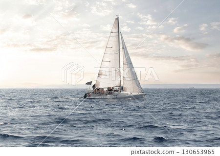 Serene sailboat cruising on calm sea waters with a soft glow of sunset 130653965