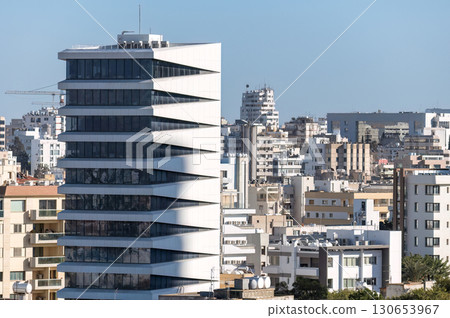 Modern office building towering over smaller residential buildings in a city center of Nicosia. Cyprus 130653967