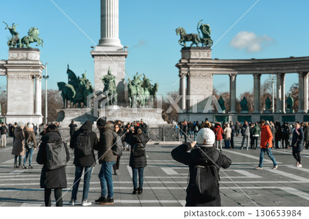 Woman taking pictures of Heroes' Square in Budapest with tourists walking around. Budapest, Hungary Woman taking pictures of Heroes' Square in Budapest with tourists walking around. Budapest, Hungary 130653984