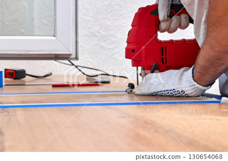 repairman using electric jigsaw and cutting hole for the sink in the kitchen countertops 130654068