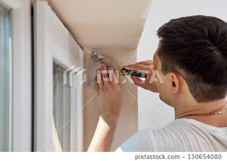 Caucasian plasterer man with a spatula applying finishing putty on a window opening Caucasian plasterer man with a spatula applying finishing putty on a window opening 130654080